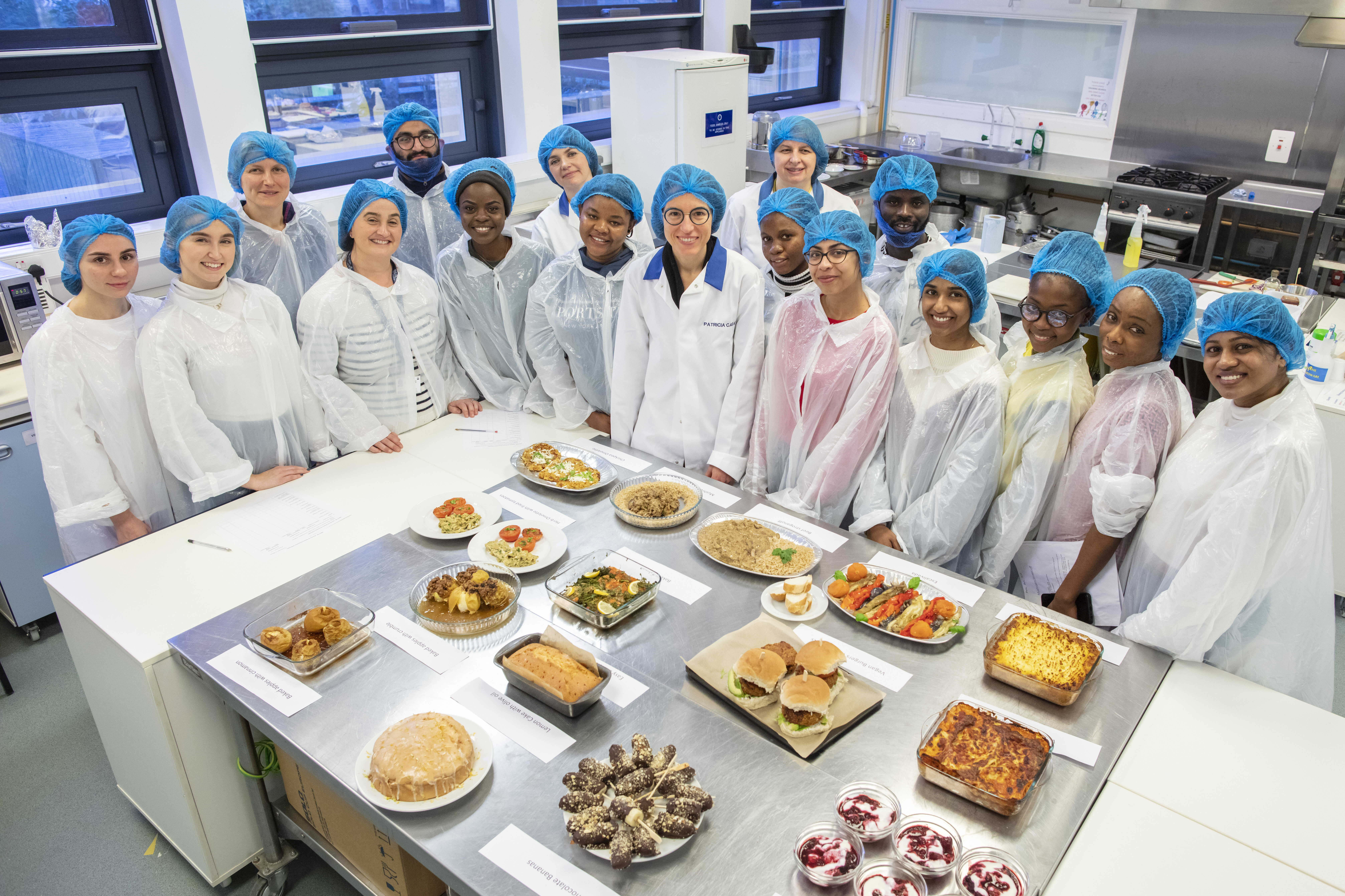 A group of young people in plastic gear stand in front of a table of food in a University food lab