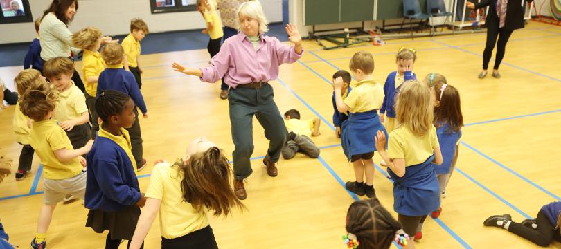 Children moving and dancing around a school hall with their teachers and facilitators