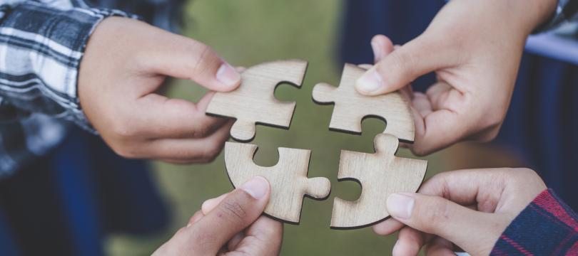 people helping in assembling puzzle, cooperation in decision making, close view of hands connecting pieces.