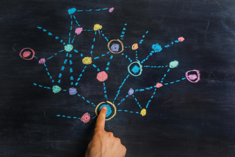 A blackboard with a colourful drawing of connected dots. A finger is pressing down on the biggest dot.