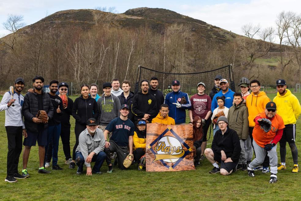 Group shot of the Edinburgh Rays baseball in playing field, standing/crouching around their logo