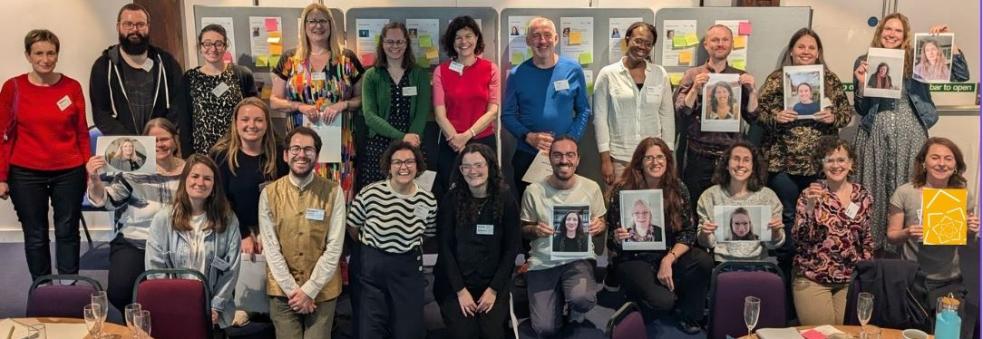 The Academy 2023_24 cohort standing/kneeling in two rows, some holding images of those not in the room