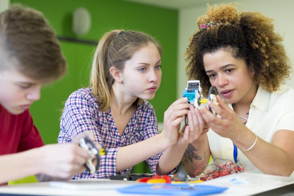 Three young people sitting around a table, examining circuit boards