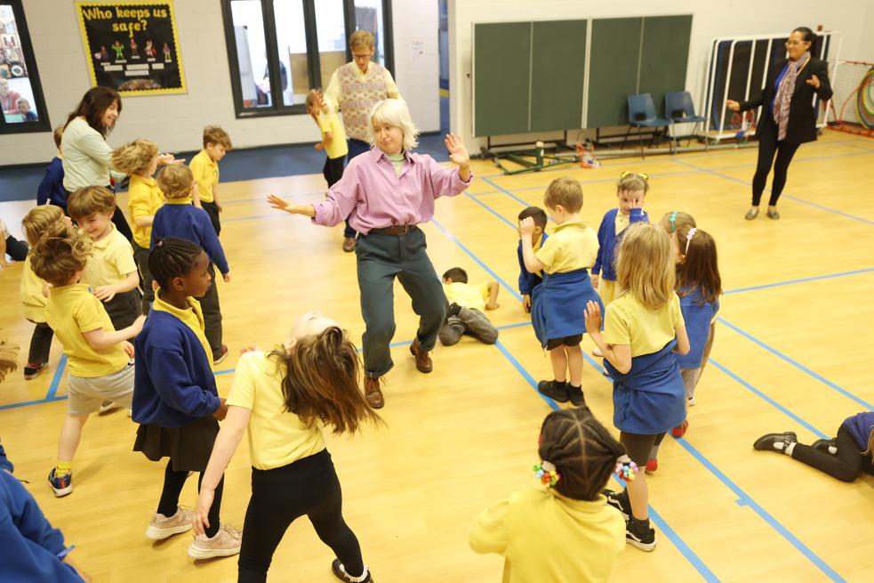 Children moving and dancing around a school hall with their teachers and facilitators