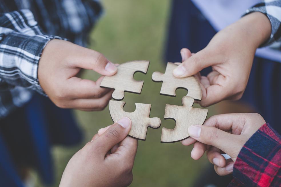 people helping in assembling puzzle, cooperation in decision making, close view of hands connecting pieces.