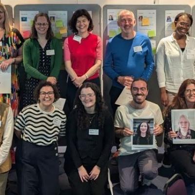 The Academy 2023_24 cohort standing/kneeling in two rows, some holding images of those not in the room