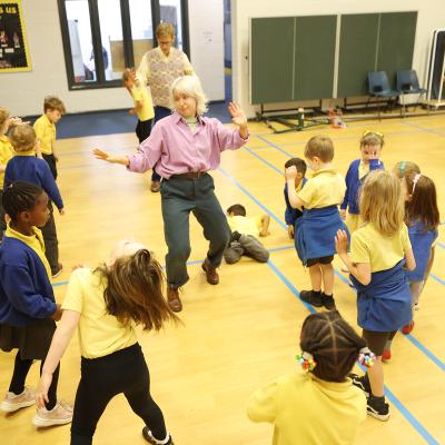 Children moving and dancing around a school hall with their teachers and facilitators