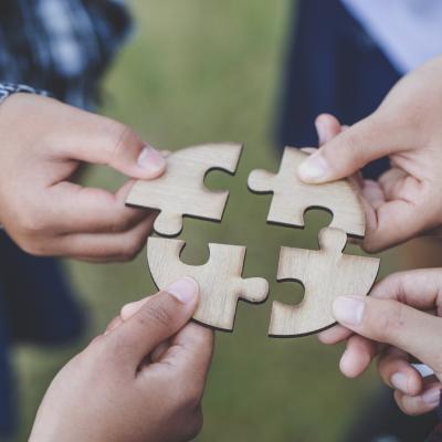 people helping in assembling puzzle, cooperation in decision making, close view of hands connecting pieces.