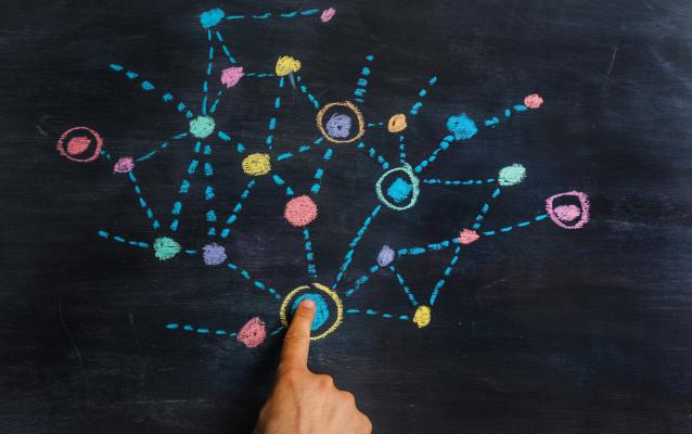 A blackboard with a colourful drawing of connected dots. A finger is pressing down on the biggest dot.