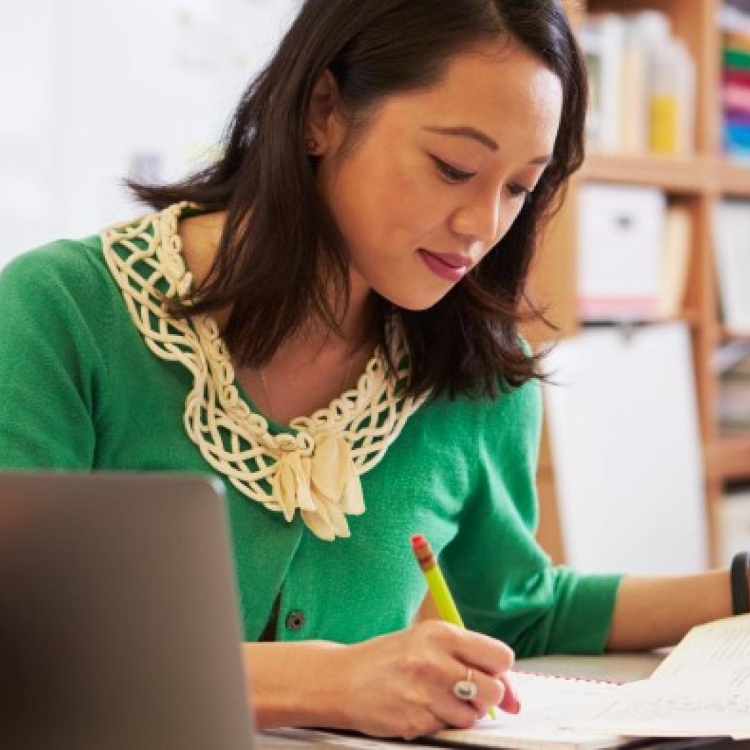 woman hand writing on form with laptop on table next to her